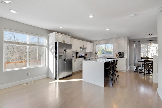 kitchen featuring visible vents, decorative backsplash, appliances with stainless steel finishes, light wood-type flooring, and under cabinet range hood