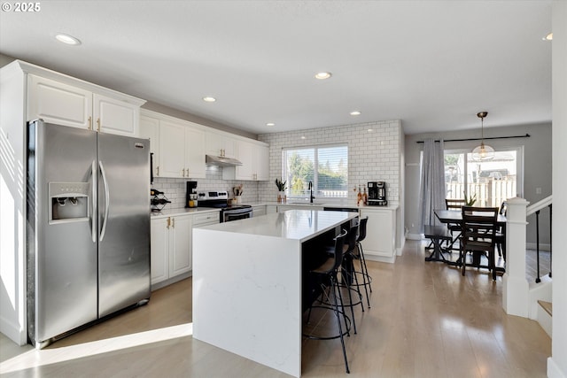 kitchen featuring stainless steel appliances, light wood-type flooring, a sink, and decorative backsplash