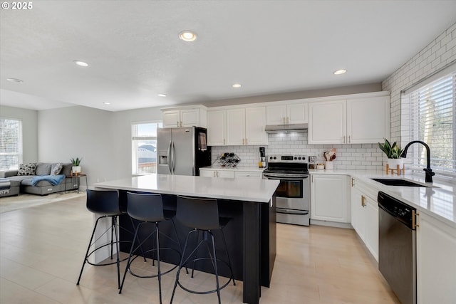 kitchen with a kitchen island, a sink, white cabinetry, a kitchen breakfast bar, and appliances with stainless steel finishes