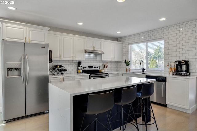 kitchen featuring tasteful backsplash, appliances with stainless steel finishes, under cabinet range hood, white cabinetry, and a sink