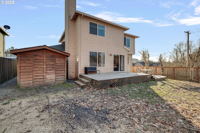 back of property with an outbuilding, a deck, a fenced backyard, a shed, and a chimney