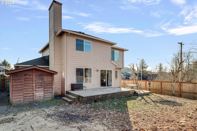 back of property featuring a storage shed, a chimney, an outbuilding, fence, and a deck