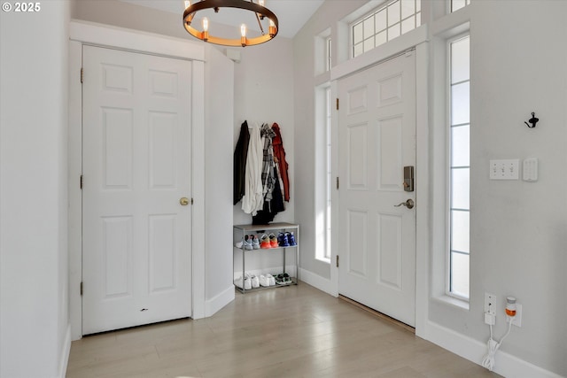 foyer featuring baseboards, light wood finished floors, and an inviting chandelier