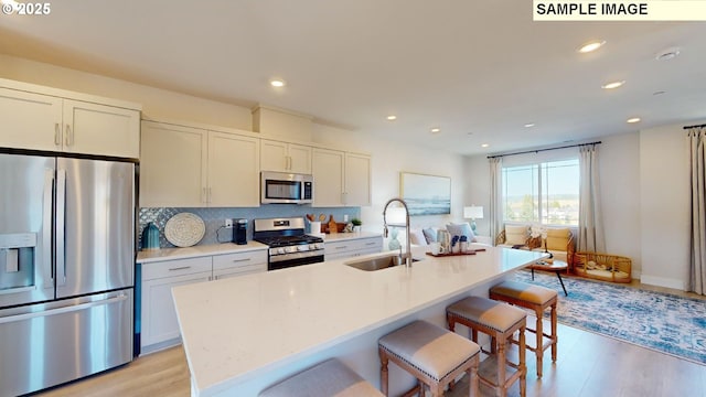 kitchen featuring white cabinetry, stainless steel appliances, a kitchen island with sink, and sink