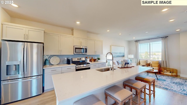 kitchen with white cabinetry, sink, stainless steel appliances, and an island with sink