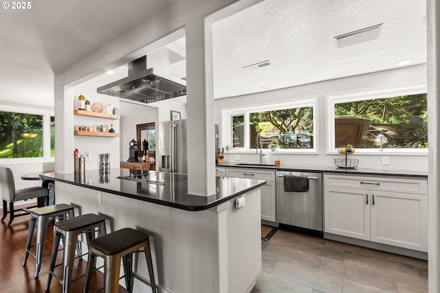kitchen featuring a breakfast bar, appliances with stainless steel finishes, dark countertops, a sink, and visible vents