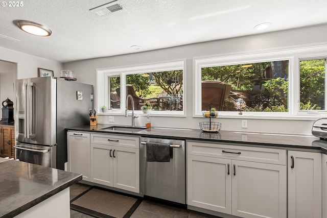 kitchen with visible vents, stainless steel appliances, dark countertops, and a sink