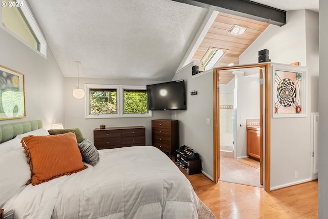 bedroom featuring baseboards, lofted ceiling with beams, ensuite bath, and light wood finished floors