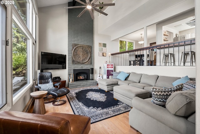 living area with high vaulted ceiling, ceiling fan, wood finished floors, and a fireplace