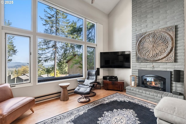 living area featuring a brick fireplace, a high ceiling, baseboard heating, and wood finished floors