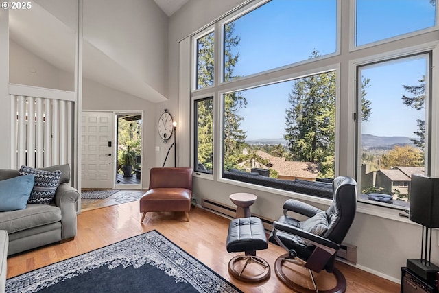 living area featuring a wealth of natural light, wood finished floors, high vaulted ceiling, and baseboard heating