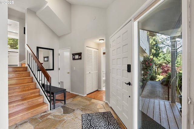 entryway with stone finish flooring, stairway, and a towering ceiling