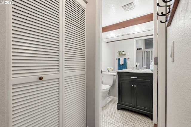 half bathroom featuring visible vents, a closet, toilet, vanity, and tile patterned flooring
