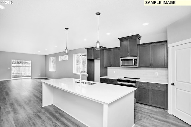 kitchen featuring a center island with sink, a sink, light countertops, light wood-style floors, and stainless steel appliances