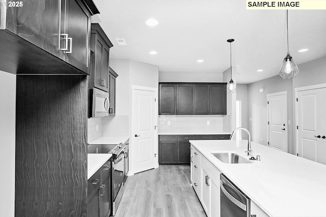 kitchen with light wood-style floors, light countertops, tasteful backsplash, a sink, and appliances with stainless steel finishes