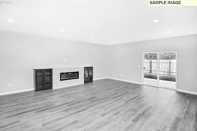 unfurnished living room featuring a glass covered fireplace, baseboards, recessed lighting, and wood finished floors