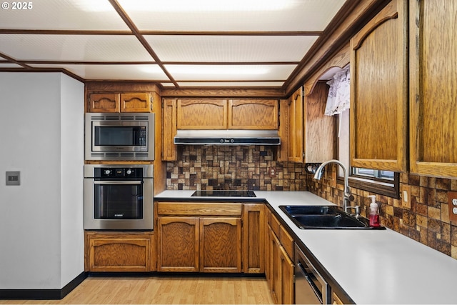 233 SE Paloma Ave, Gresham, OR 97080 - kitchen with appliances with stainless steel finishes, under cabinet range hood, tasteful backsplash, brown cabinetry, and light wood-style flooring