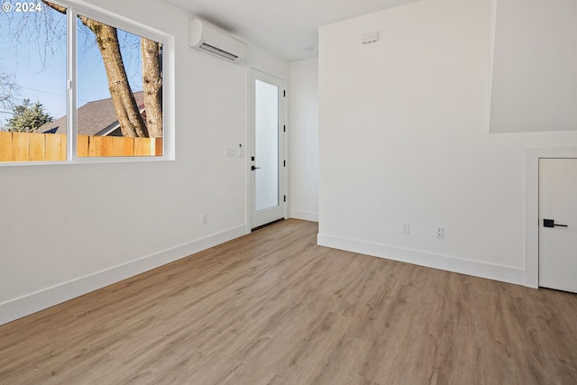 unfurnished room with a wall mounted air conditioner, baseboards, and wood finished floors