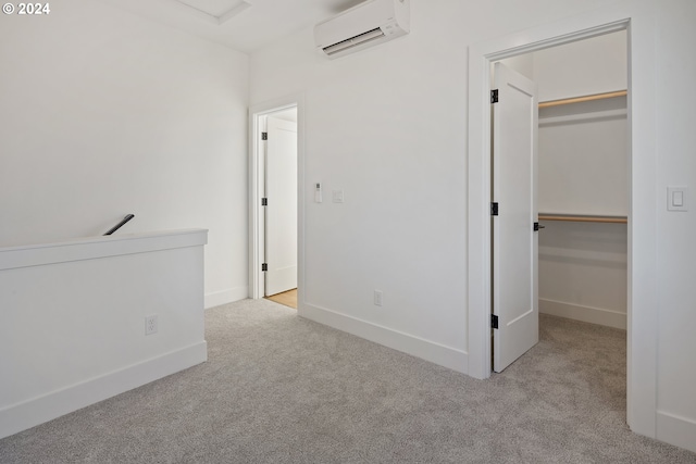 unfurnished bedroom with a wall mounted AC, carpet flooring, a walk in closet, and baseboards