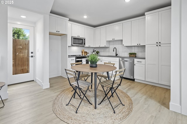 kitchen featuring tasteful backsplash, dark countertops, appliances with stainless steel finishes, light wood-style floors, and a sink