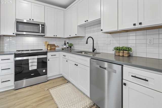 kitchen with dark countertops, stainless steel appliances, light wood-type flooring, white cabinetry, and a sink