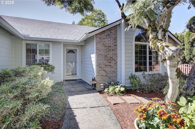 entrance to property featuring brick siding and roof with shingles