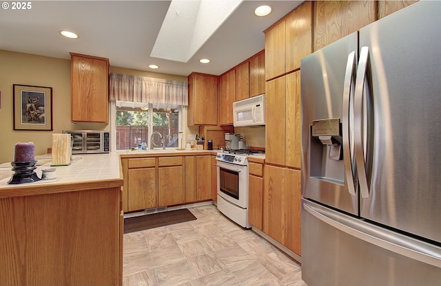 kitchen featuring a skylight, tile counters, recessed lighting, a sink, and white appliances