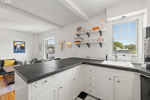 kitchen with kitchen peninsula, dishwashing machine, sink, beamed ceiling, and white cabinets