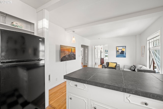 kitchen featuring black refrigerator, decorative light fixtures, light hardwood / wood-style flooring, and white cabinetry