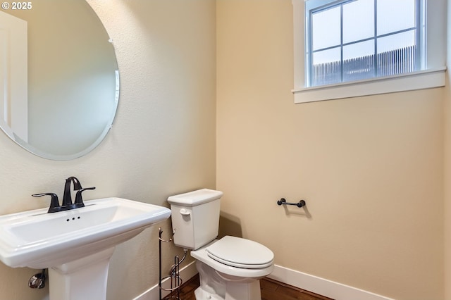 half bathroom featuring a sink, baseboards, toilet, and wood finished floors