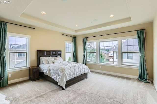 bedroom featuring light colored carpet, a raised ceiling, baseboards, and multiple windows