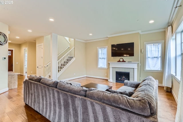 living area with stairs, wood finished floors, ornamental molding, and a fireplace