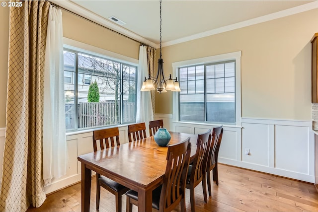 dining space featuring visible vents, a wainscoted wall, ornamental molding, an inviting chandelier, and light wood finished floors