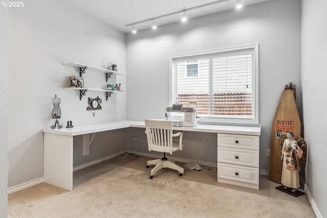 office space with baseboards, light carpet, rail lighting, and built in desk