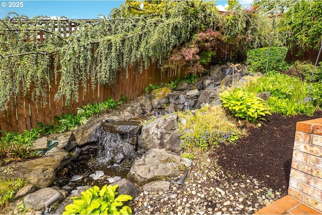 view of yard featuring fence and a garden pond