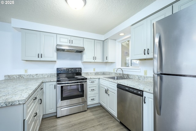 kitchen featuring light wood-style flooring, appliances with stainless steel finishes, light countertops, under cabinet range hood, and a sink