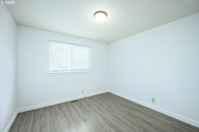 empty room featuring visible vents, a textured ceiling, baseboards, and wood finished floors