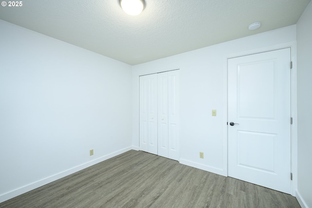 unfurnished bedroom with a textured ceiling, a closet, baseboards, and wood finished floors