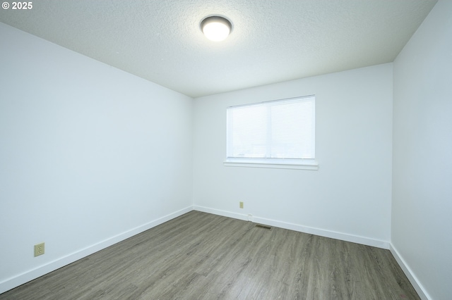 spare room with visible vents, a textured ceiling, baseboards, and wood finished floors