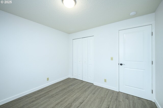 unfurnished bedroom featuring a closet, a textured ceiling, baseboards, and wood finished floors