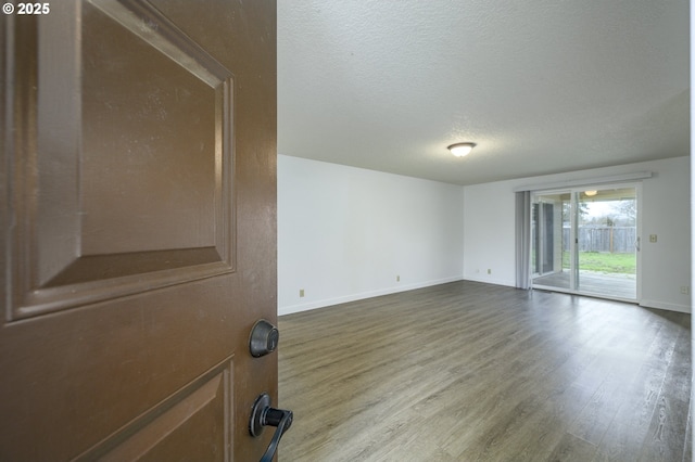 spare room featuring a textured ceiling, wood finished floors, and baseboards