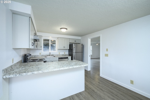 kitchen with dark wood finished floors, light countertops, appliances with stainless steel finishes, a sink, and a peninsula