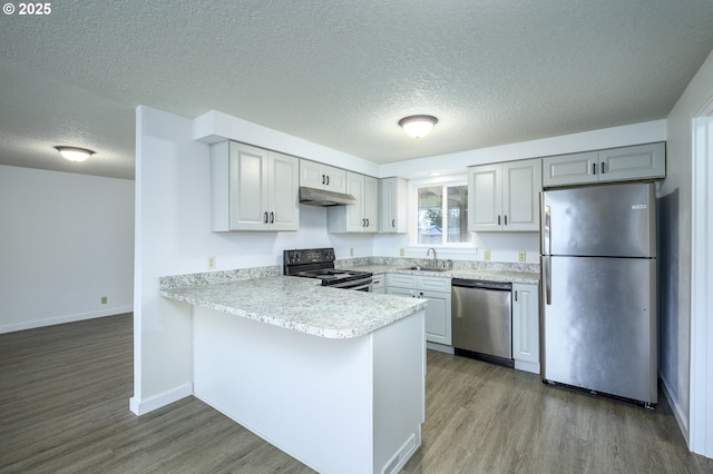 kitchen with under cabinet range hood, stainless steel appliances, wood finished floors, a sink, and light countertops