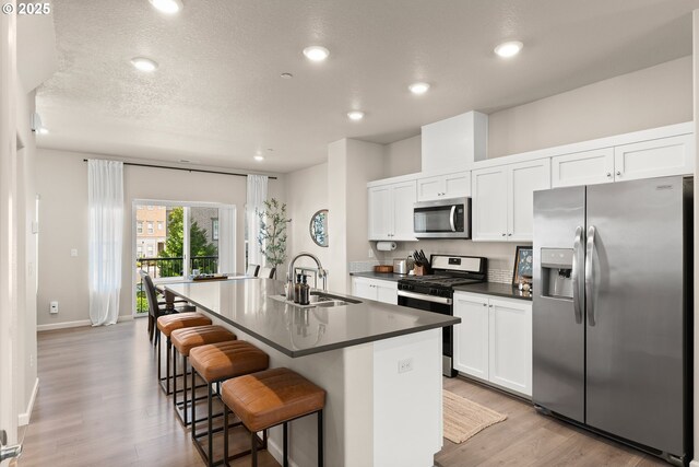 11469 SW Mont Blanc St, Wilsonville, OR 97070 - kitchen featuring appliances with stainless steel finishes, an island with sink, light wood-style flooring, dark countertops, and a breakfast bar