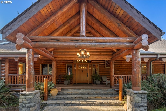 doorway to property with covered porch, log exterior, and a shingled roof