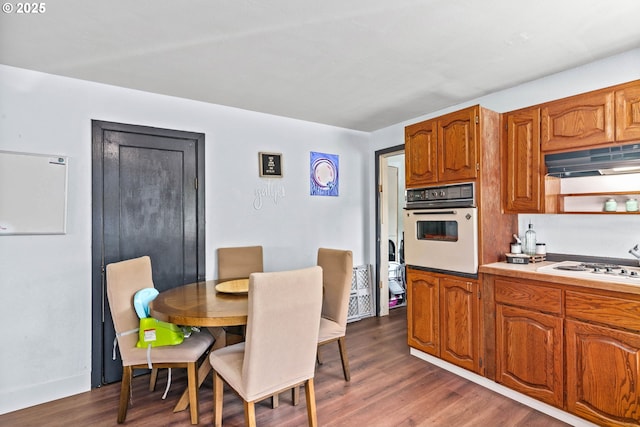 1483 5th St, Springfield, OR 97477 - kitchen with white appliances, under cabinet range hood, brown cabinetry, dark wood-style flooring, and light countertops