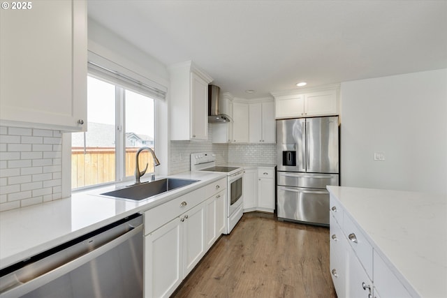 kitchen with stainless steel appliances, wall chimney range hood, white cabinets, wood finished floors, and decorative backsplash