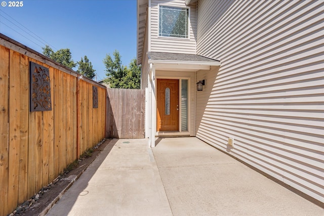 entrance to property featuring roof with shingles and a patio