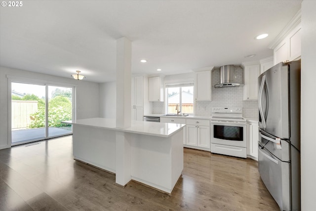kitchen with appliances with stainless steel finishes, wall chimney range hood, decorative backsplash, light countertops, and white cabinets
