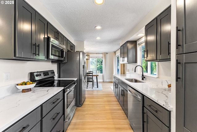 kitchen with recessed lighting, light wood-style flooring, appliances with stainless steel finishes, a sink, and a textured ceiling